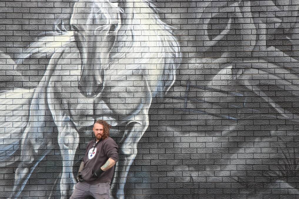Joe Quilter, who stands with a mural created for Paint the Town in Tahmoor, is coming to the Highlands to create a unique mural for the Paint the Town Laneway Festival. Picture supplied. 