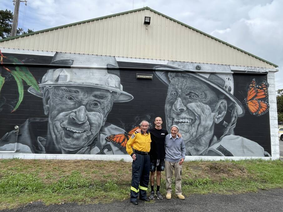 Rural Fire Service volunteers Brian Coates (left) and John Matters (right) with artist Samuel Hall who painted them for a mural on the side of Hill Top's fire station. Picture by Briannah Devlin